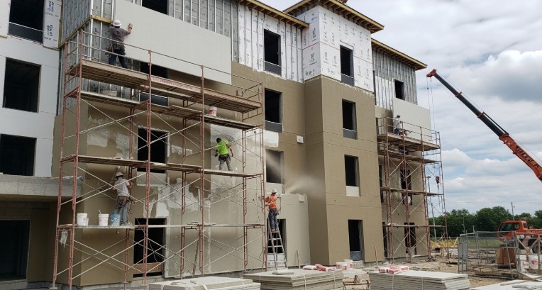 Hotel building under construction with workers installing EIFS exterior insulation panels and applying finish coating on multi-story façade